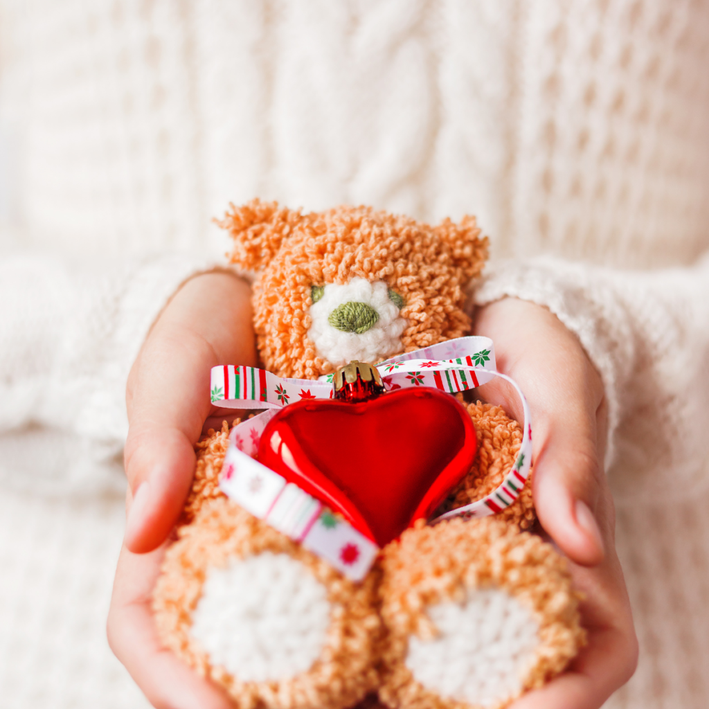 Person holding in their hands a plush bear toy with red heart for Valentine's Day.