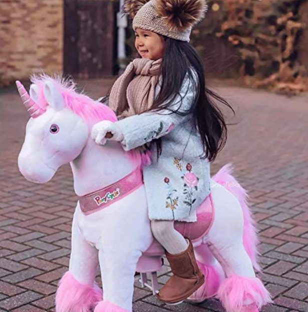 Little girl riding on a pink unicorn rocking horse.